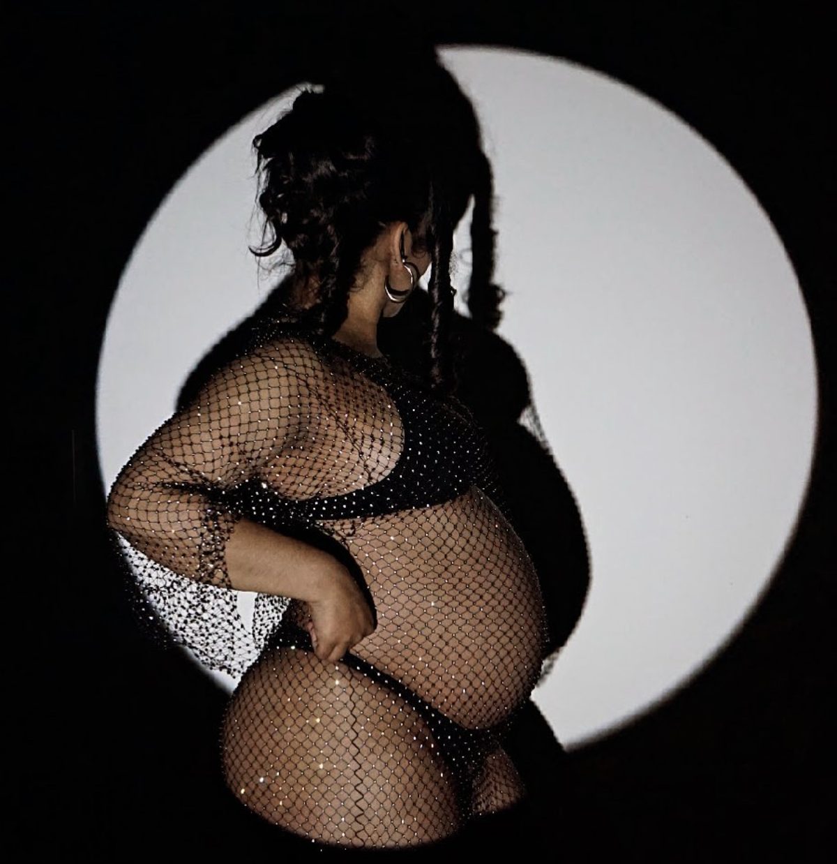Her silhouette in profile against a round white spotlight, hand on her hip.