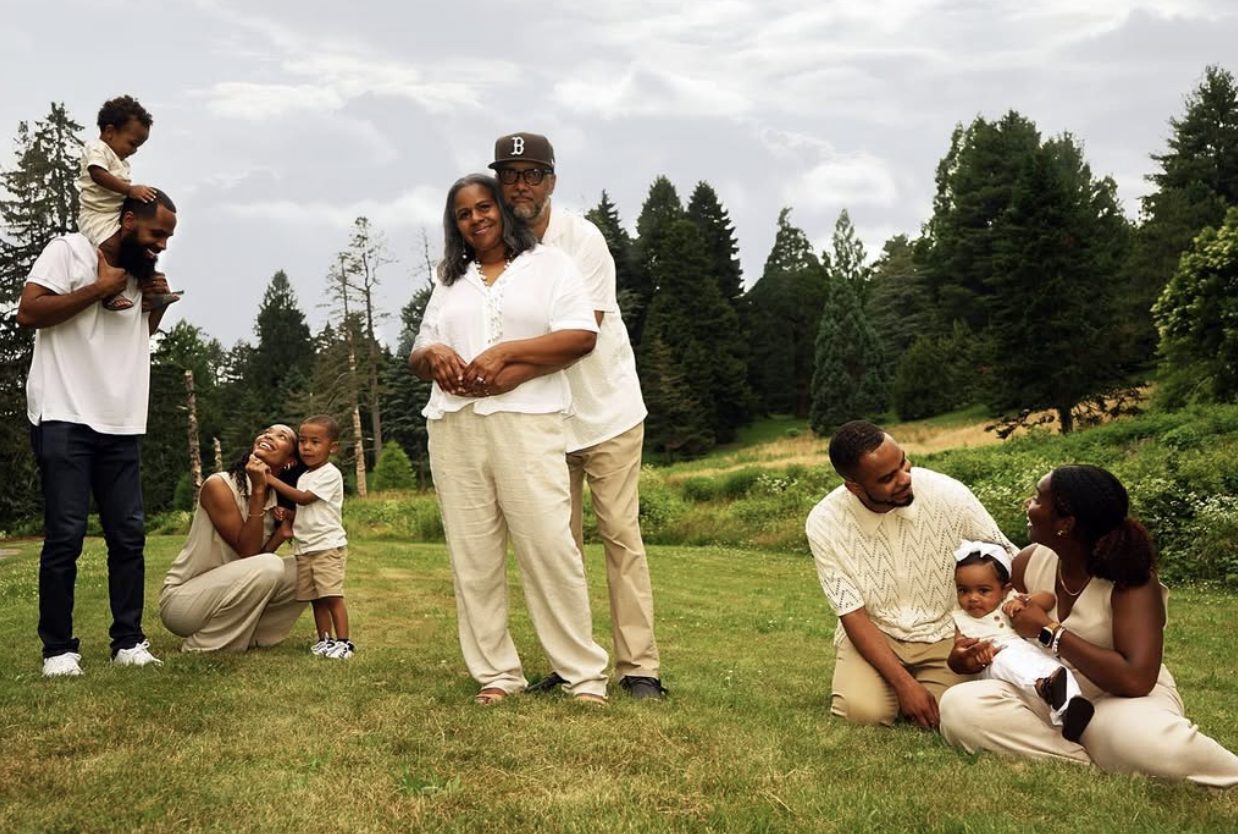 The grandparents embrace at the center while their children and grandchildren play around them.